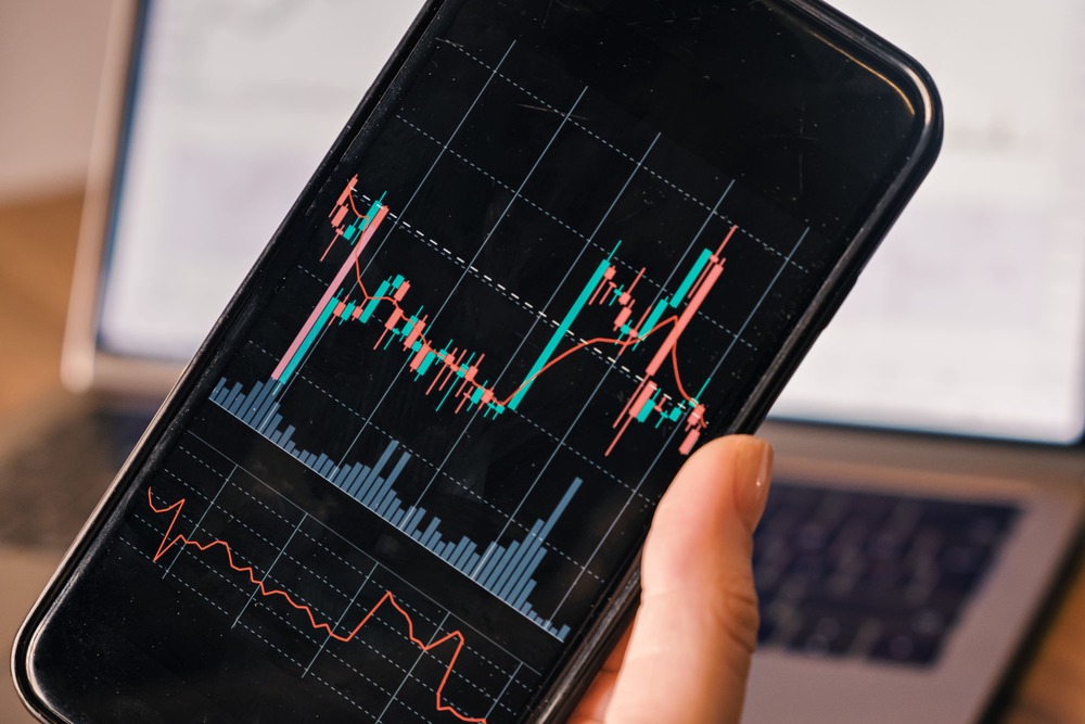 hand holding smart phone with candle graph for tra